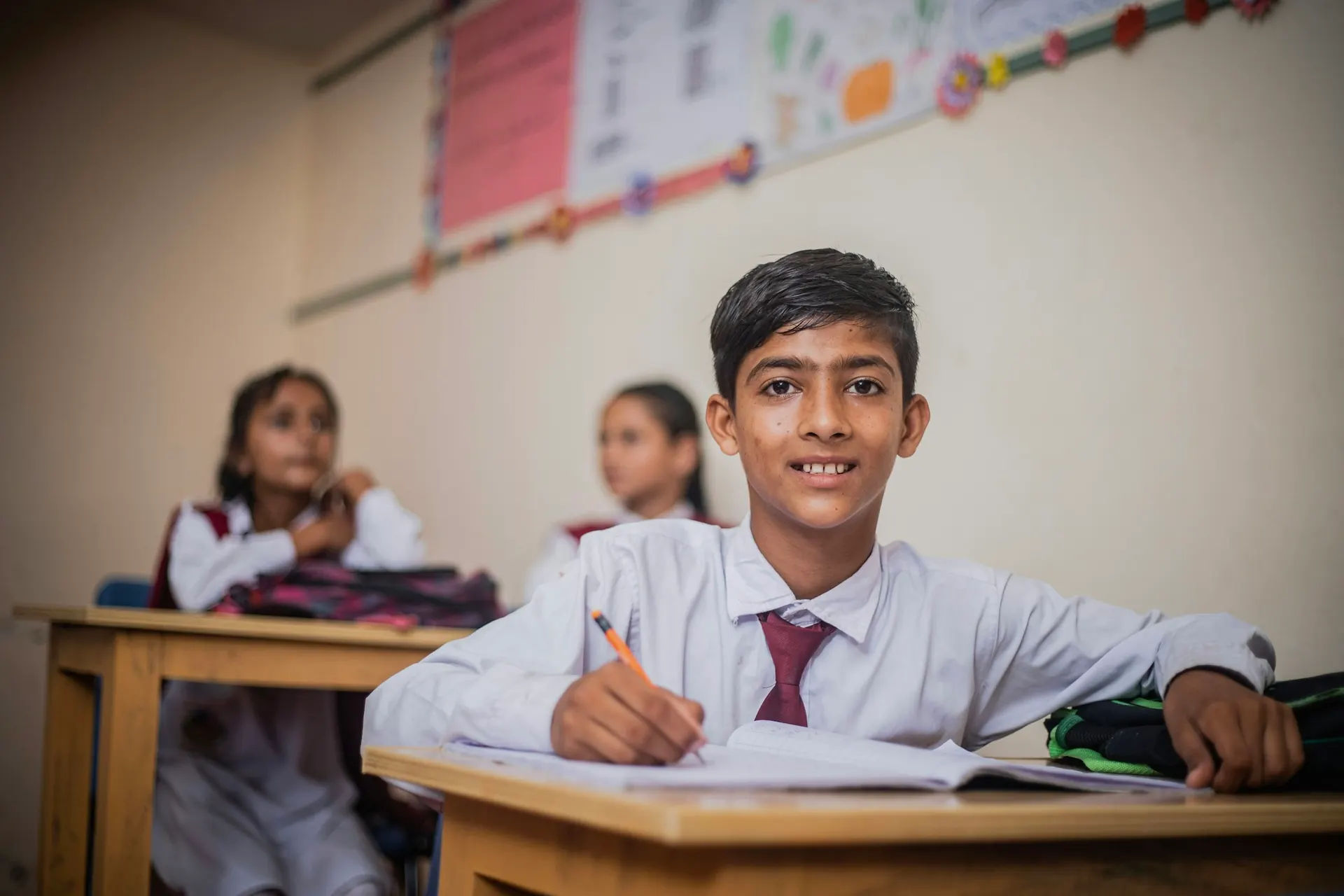 Student in school uniform writing in his notebook at his desk
