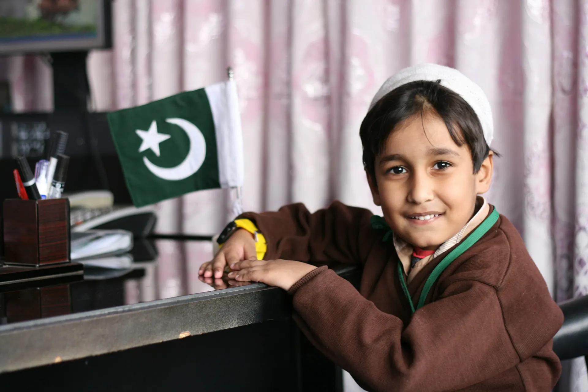 Student in uniform at his desk beside a Pakistan flag